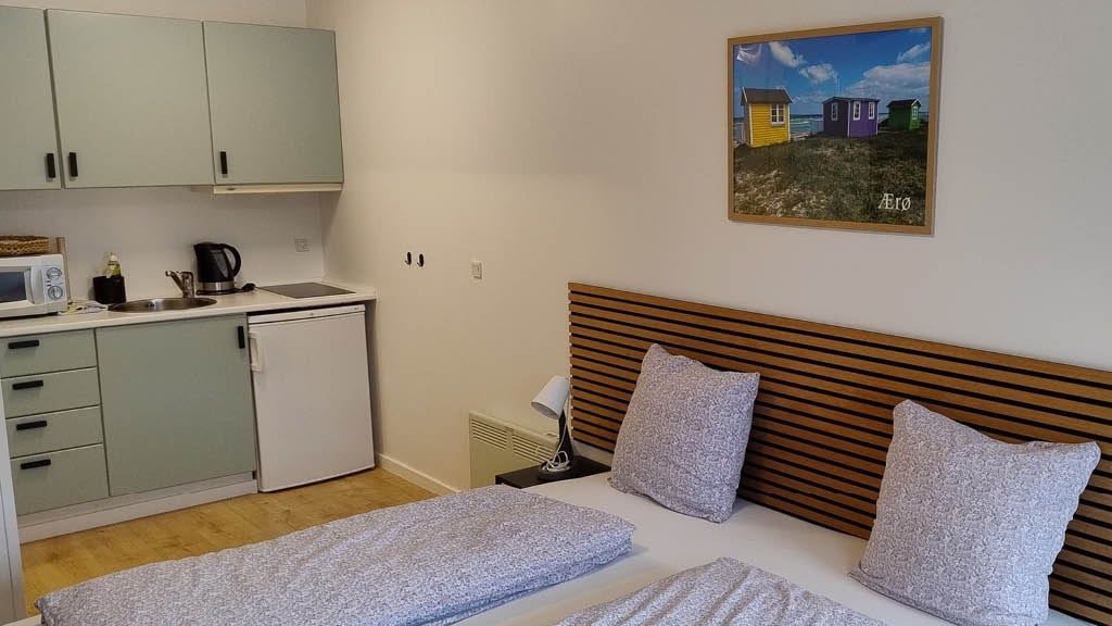 Åbent tekøkken ved sengeområdet med Ærø-plakat over sengen
