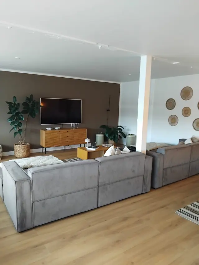 Perlen — Åben stue med to store grå modulsofaer, teaksideboard og fladskærm