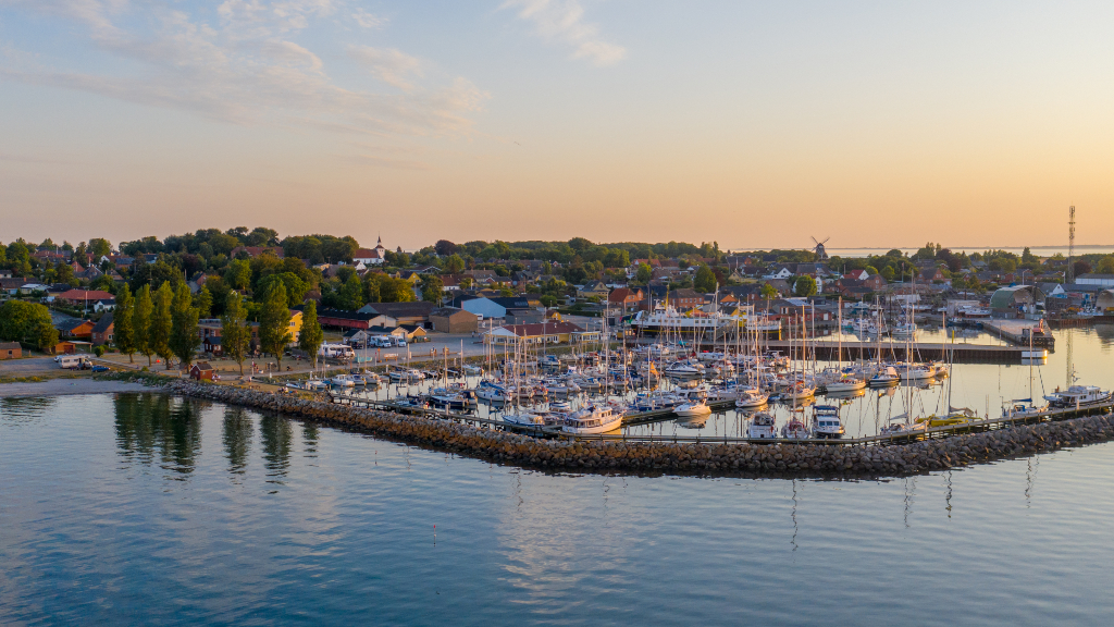 Søby Havn i solnedgang set fra luften med lystbåde, husene langs vandet og møllen i horisonten